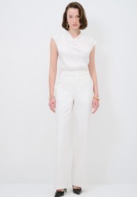 Blusa blanca sin mangas con cuello drapeado, combinada con pantalones de pierna ancha de talle alto. Textura de tela suave, diseño minimalista y tacones negros.