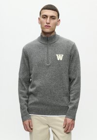 Gray pullover sweater with a high collar, front zipper, and ribbed cuffs. Features a contrasting cream logo on the chest. Soft, textured fabric.