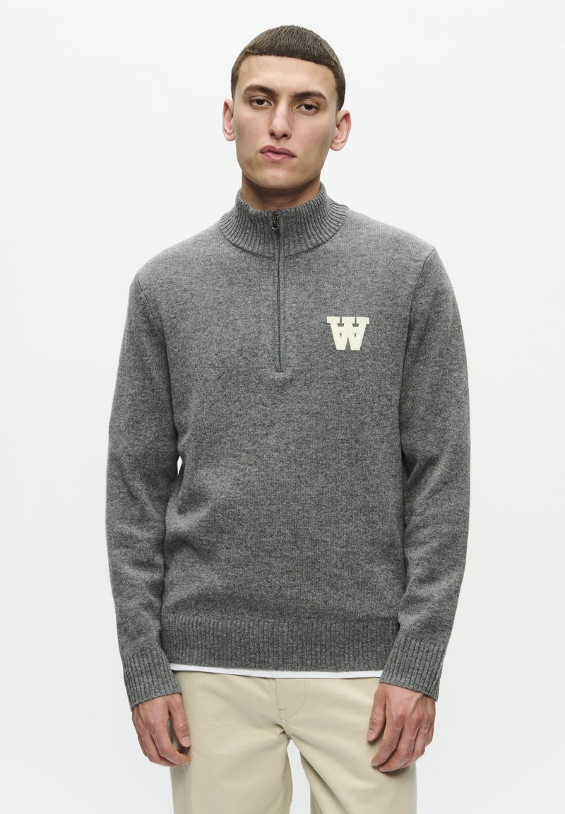 Gray pullover sweater with a high collar, front zipper, and ribbed cuffs. Features a contrasting cream logo on the chest. Soft, textured fabric.