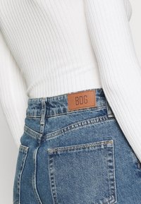 Lättvikts, ribbad vit topp matchad med högmidjade blå denimjeans som har en brun läderetikett från BDG på baksidan av midjan.