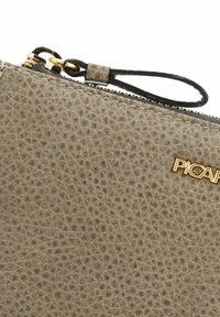 Getextureerde taupe leren pouch met gouden ritssluiting en zwarte polsband, voorzien van kleine gouden merknaam letters op de voorkant.