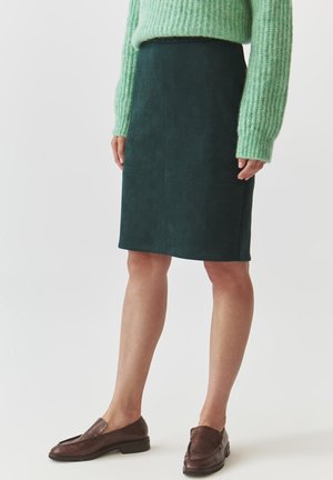 Gonna a matita in suede verde scuro con una texture liscia, caratterizzata da una silhoutte aderente e dettagli sulle cuciture laterali. Abbinata a un maglione a coste verde chiaro.
