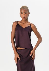 Burgunder sateng singlet med tynne stropper, v-halsdesign, myk tekstur, flytende passform, kombinert med et matchende skjørt.