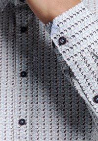 Lange mouwen shirt in lichtblauw met een ingewikkeld zwart-wit patroon. Bevat donkere knopen bij de manchetten en de kraag, gemaakt van een zachte stof.