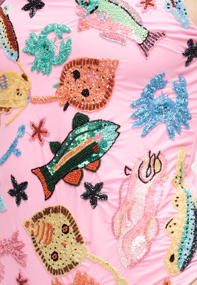 Πολύχρωμα θαλάσσια πλάσματα από χάντρες, όπως ψάρια, σαλάχια, καβούρια και αστερίες, πάνω σε ανοιχτό ροζ υφασμάτινο φόντο.