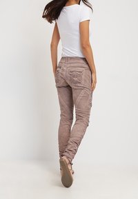 Jasnobrązowe spodnie cargo o wąskim kroju, z widocznymi przeszyciami i zapinanymi na guziki tylnymi kieszeniami, zestawione z dopasowanym białym t-shirtem.