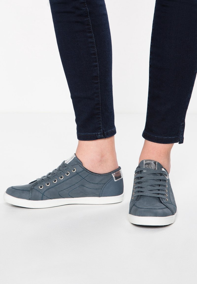 Grå sneakers gjorda av texturerat material med vita sulor. Har rund tå, snörning och metallöglor. Diskreta accenter vid hälen.