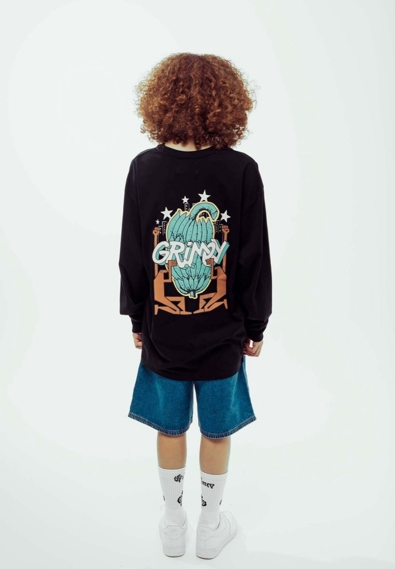 Svart långärmad tröja med grafisk design i gröna inslag och ordet "GRIMY" på ryggen, tillsammans med denimshorts och vita strumpor.