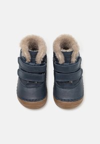 Marineblå lædersko med blød beige imiteret pelsforing, dobbelt velcro-stropper og brune gummisåler. Rund tåform, syede detaljer.