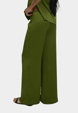 Pantaloni a gamba larga in tessuto ribbed verde oliva, con un design a vita alta e una texture liscia, abbinati a sandali neri.