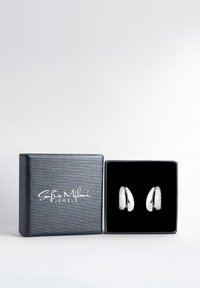 Silverfärgade örhängen i en svart sammetssäkrad box, med oval form och strukturerade detaljer, uppvisade mot en ljus bakgrund.