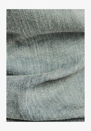 Ljust blå denimtyg med en twillväv, som har en mjuk textur och subtila färgvariationer, som visar vikta och lager-på-lager sektioner.