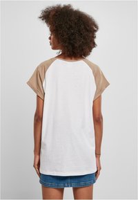 Hvit og beige raglan T-skjorte med korte ermer, med rund halslinning og avslappet passform. Myk bomullsblanding med glatt tekstur.