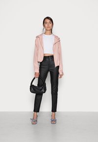 Casaco cropped, com capuz, em rosa claro e com fecho, combinado com calças pretas de cintura alta. Uma mala trançada preta e sapatos de salto quadrados completam o visual.