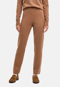 Brązowe dzianinowe spodnie o gładkiej fakturze i zwężanym kroju, z wysokim paskiem i prążkowanymi akcentami. Połączone z brązowymi butami wsuwanymi.