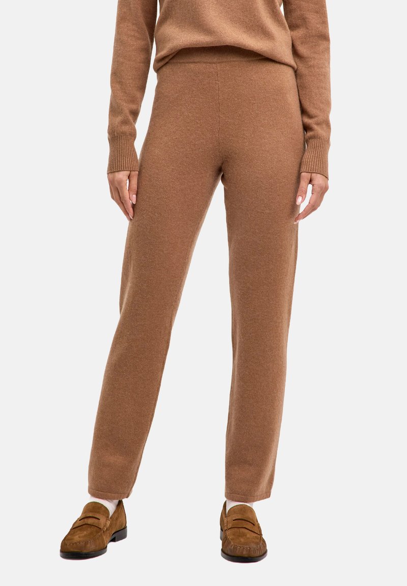 Brązowe dzianinowe spodnie o gładkiej fakturze i zwężanym kroju, z wysokim paskiem i prążkowanymi akcentami. Połączone z brązowymi butami wsuwanymi.