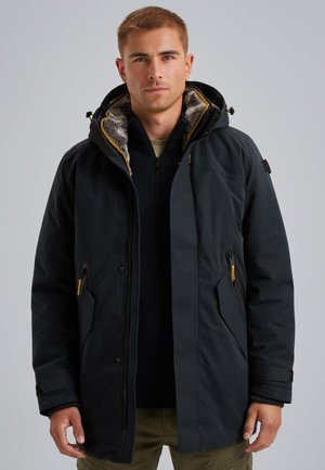 Donkerblauwe geïsoleerde parka met een met bont gevoerde capuchon, ritszakken en gele accenten. Beschikt over een stevige stof en een comfortabele pasvorm.