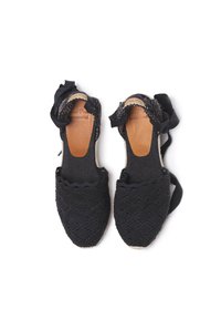 Espadrillas nere all'uncinetto con bordo a onde, punta arrotondata e lacci in tessuto alla caviglia. Suola in materiale naturale per flessibilità e supporto.