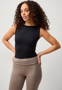 Top nero senza maniche realizzato in tessuto elastico, abbinato a leggings beige a vita alta con una fascia ripiegata in vita.