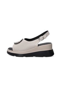 Beige slingback sandaler med perforeret overdel, rund tå og en kraftig sort sål. Udstyret med en metallisk detalje og justerbar rem.