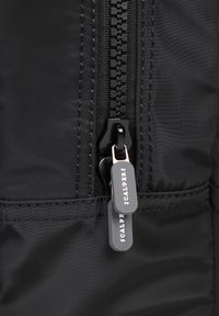 Prenda negra con cremallera que presenta un acabado texturizado, con un detalle en la costura lateral y tiradores de cremallera de la marca "SCALPERS".