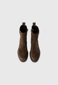 Stivali ankle in suede marrone con punta tonda e cerniera laterale. Presentano una suola in gomma nera resistente e un loop sul tallone.