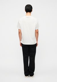 Λευκό βαμβακερό μπλουζάκι με κοντά μανίκια, απλό στρογγυλό λαιμό, σε συνδυασμό με μαύρο παντελόνι και ανοιχτόχρωμα αθλητικά παπούτσια. Εφαρμοστή γραμμή, μινιμαλιστικός σχεδιασμός.