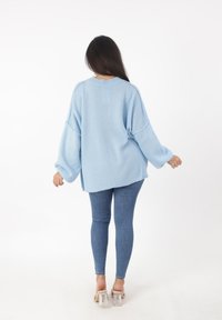 Hellblaues, übergroßes Sweatshirt mit herunterhängenden Schultern, gerippter Textur und seitlichen Schlitzen, kombiniert mit engen Jeans und Schuhen mit transparenten Absätzen.