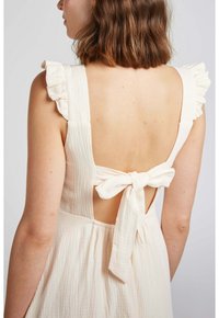 Robe couleur crème avec un tissu texturé, des bretelles volantées, un dos nu et un détail à nouer à la taille.
