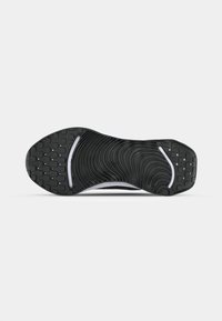 Semelle de chaussure noire avec motif de bande de roulement structuré, comprenant des lignes courbes au centre et des zones de préhension carrées aux orteils et au talon.