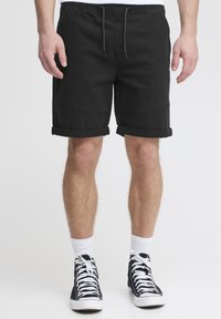 Shorts en coton noirs avec une taille à cordon de serrage, des ourlets roulés, des coutures latérales et une coupe décontractée, portés avec des baskets montantes noires et des chaussettes blanches.