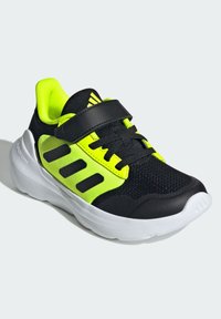 Schwarzer und neongrüner Sportschuh mit Mesh-Obermaterial, Klettverschluss und weißer Sohle. Verfügt über drei schwarze Streifen und strukturierte Akzente.