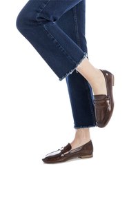 Mocasines de charol marrón con un acabado suave, que presentan un acento de costura. Combinados con unos vaqueros oscuros de mezclilla con dobladillos deshilachados.