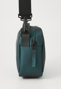 Borsa impermeabile color turchese con finitura opaca, dotata di chiusura a zip e tracolla nera regolabile. Forma rettangolare con superficie liscia.