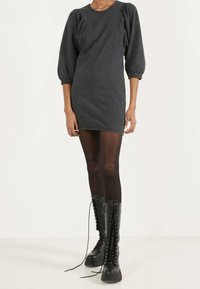 Vestido mini de denim oscuro con manga abullonada, costuras en las costados, combinado con botas negras de caña alta con cordones y medias negras.