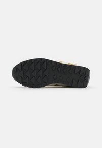 Witte en crème sneakerzool met opvallende zwarte gripnoppen, een getextureerd rubberen oppervlak en een subtiel logo dat aan de zijkant is geperst.