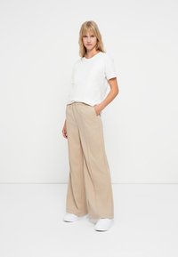 Hvit bomull T-skjorte med løs passform, kombinert med beige bukser med vid benvidde, elastisk liv og sidelommer. Hvit sneakers.