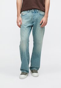 Ανοιχτό μπλε τζιν, άνετη εφαρμογή, ξεθωριασμένο μπροστινό μέρος, σχεδιασμός με πέντε τσέπες, μεταλλικά εξαρτήματα και ραφές λεπτομέρειες. Φορεμένο με γκρι αθλητικά παπούτσια.