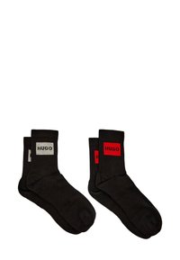 Calcetines negros con parches de logotipo rectangulares en rojo y gris que contrastan. Puños acanalados con textura suave.