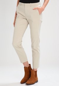 Ljust beige skräddarsydda byxor med smal passform, med sidofickor och en mjuk textur, kombinerat med bruna mocka stövletter.