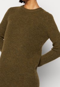 Olijfgroene gebreide trui met een ronde hals, lange mouwen en een ontspannen pasvorm; het gestructureerde materiaal geeft een zachte uitstraling en een warme feel.