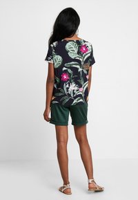 Czarny t-shirt z krótkim rękawem z kolorowym nadrukiem kwiatowym; połączony z zielonymi szortami. Sandały dopełniają casualowy strój.