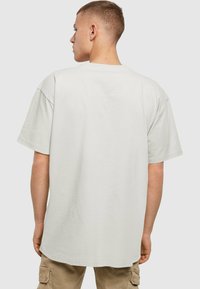 Camiseta blanca de gran tamaño con mangas cortas, hecha de algodón, con un cuello redondo y una textura suave. Vista trasera mostrada.