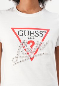T-shirt in cotone bianco con un logo triangolare rosso che presenta la scritta "GUESS USA" e decorato con un design scintillante della parola "love" in perline.