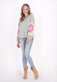 Ljusgrön sweatshirt med långa, mönstrade ärmar som har pastellblommor; kombinerad med ljus tvättade jeans och beige cowboystövlar.