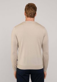 Maglione beige a maniche lunghe con una texture liscia, polsini e orlo a coste e una vestibilità rilassata. Presenta un piccolo dettaglio del logo sul lato.