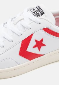 Tenisi din piele albă cu accente de design din stea roșie și chevron. Șireti albi, talpă din cauciuc și etichetă de marcă pe limbă. Textură netedă.