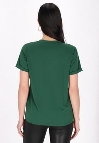 Grön kortärmad t-shirt med rund halsringning; tillverkad av mjukt tyg med en avslappnad passform och uppvikta ärmar. Enkel, odekorerad bakvy.