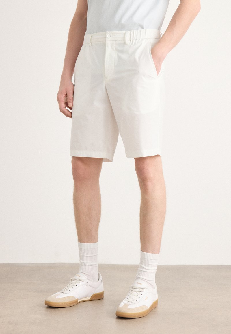 Shorts en coton blancs avec une taille élastique, dotés de deux poches latérales. Associés à des baskets blanches et des chaussettes côtelées.