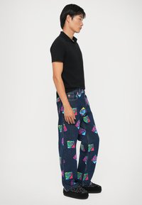 Blugi din denim albastru cu imprimeuri grafice colorate ce prezintă fețe de desene animate. Asortați cu un polo negru cu mânecă scurtă și pantofi negri cu model.
